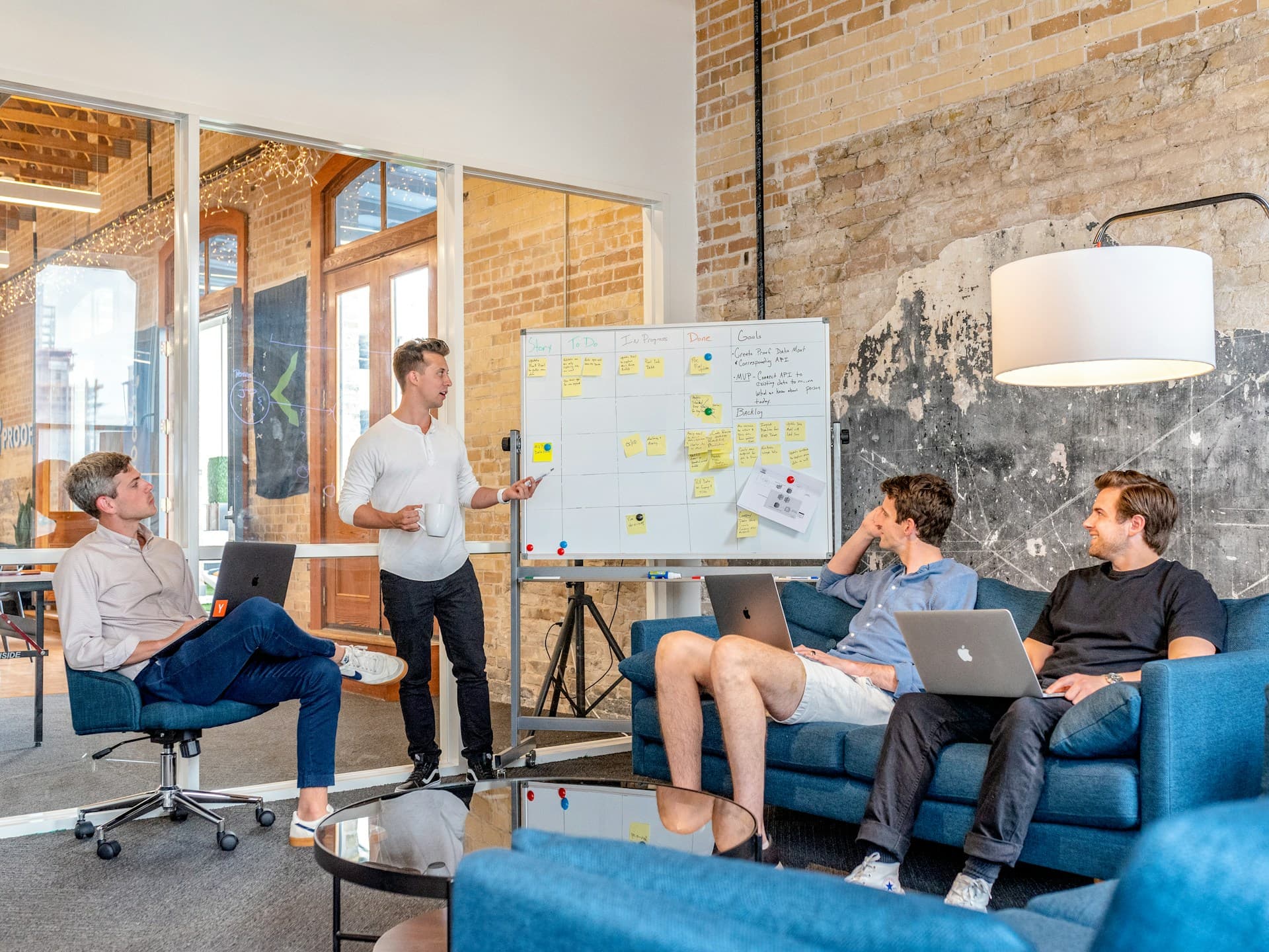 Man giving a presentation to colleagues using a whiteboard covered with sticky notes in a modern office setting.