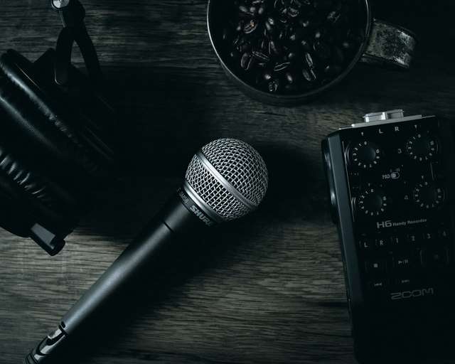 Microphone, headphones, and audio recorder on a wooden table with a cup of coffee beans - tools for recording speeches or podcasts.